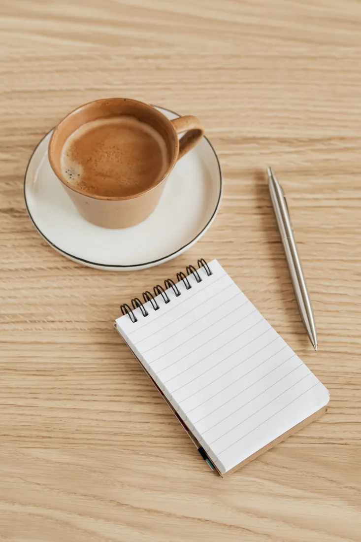 Filiżanka kawy, notes i długopis na jasnym stole